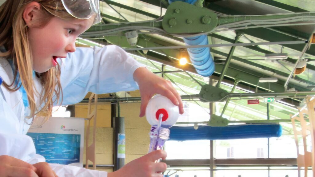 Bambina con vestito da chimico scienziato versa del liquido durante un laboratorio didattico ad Explora