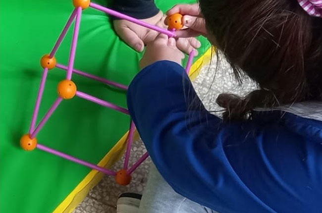 Bambina gioca con un dado costruito con cannucce durante un laboratorio didattico